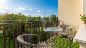 A balcony with a table and chairs, a power outlet, and a view of greenery and buildings. - Nowa Huta Charming Apartment (Kraków)