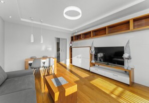 Un salon moderne avec un canapé, une table basse, un téléviseur et un plancher en bois.