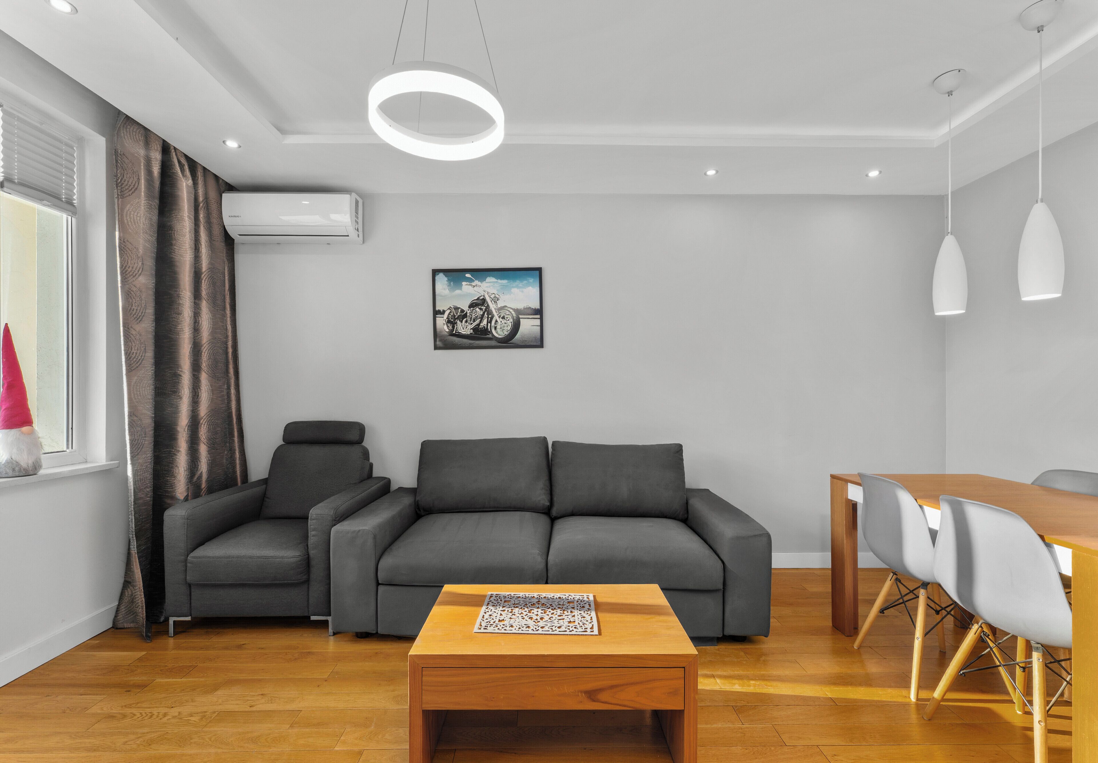 Una sala moderna con un sofá gris, una mesa de centro de madera y un comedor con una mesa de madera y sillas grises.
