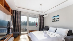A modern hotel room with a large bed, a TV, a sofa, and a balcony with a view. - Nowa Huta Charming Apartment (Kraków)