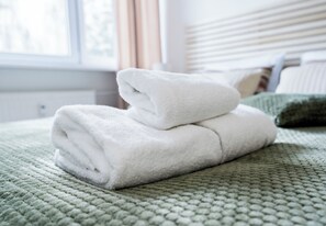 A neatly folded white towel on a textured green bedspread in a hotel room. - Krakowska Downtown Deluxe Apartment (Poznań)
