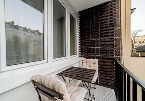 A balcony with a wooden table and two striped chairs, large windows, and a wooden slatted wall. - Krakowska Downtown Deluxe Apartment (Poznań)