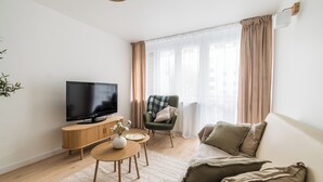 A modern living room with a flat-screen TV, wooden furniture, a green armchair, and a large window with curtains. - Krakowska Downtown Deluxe Apartment (Poznań)