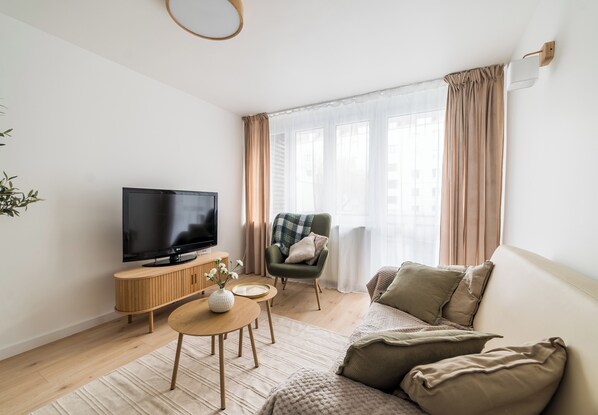A modern living room with a flat-screen TV, wooden furniture, a green armchair, and a large window with curtains. - Krakowska Downtown Deluxe Apartment (Poznań)