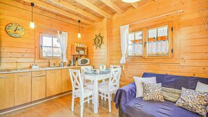 Interior de una cabaña de madera con comedor, cocina y un sofá con cojines.