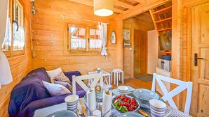 Interior acogedor de una cabaña de madera con comedor, sofá y cocina visible a través de una puerta abierta.