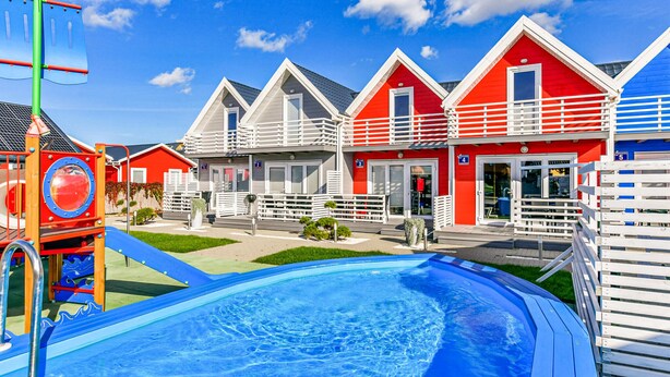 Une rangée de maisons de vacances aux couleurs vives, avec une piscine au premier plan.