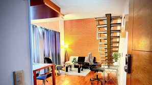 Un espacio habitable pequeño con piso de madera, un sofá, una mesa de comedor y una escalera.