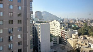Un edificio de gran altura con múltiples unidades de aire acondicionado en el exterior, una combinación de edificios residenciales y comerciales al fondo, y un paisaje montañoso.
