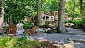 A cabin with a deck, surrounded by trees and a gravel path.