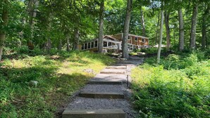 A wooden cabin with a stone staircase leading to a porch, surrounded by dense forest.