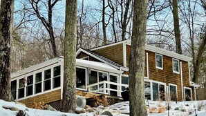 Une maison à deux étages, dotée de grandes fenêtres et d’une façade en bois, entourée d’arbres et de neige.