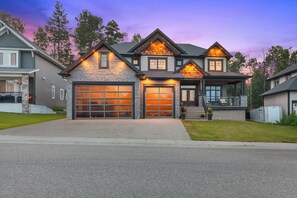 A modern two-story house with a stone facade, large garage doors, and a well-maintained lawn. - Welcome to Hearthside Estate, a 5BR, 4BA luxury retreat (CPG)