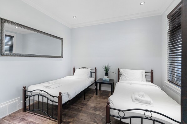 A hotel room with two single beds, a small table with a plant, and a large mirror on the wall.