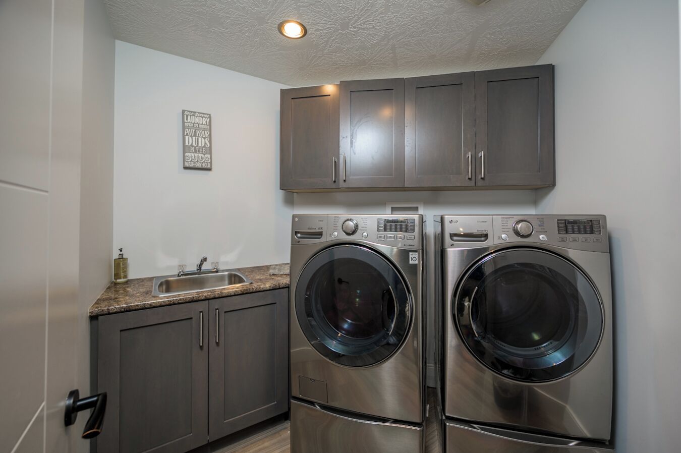 A laundry room with two stainless steel front-loading washers and a sink.