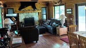L’intérieur d’une cabane en rondins, avec une cheminée, un canapé en cuir, une table à manger et un ventilateur de plafond.