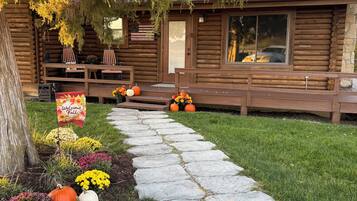 A wooden cabin with a stone pathway leading to the entrance, surrounded by autumnal foliage and decorative pumpkins.