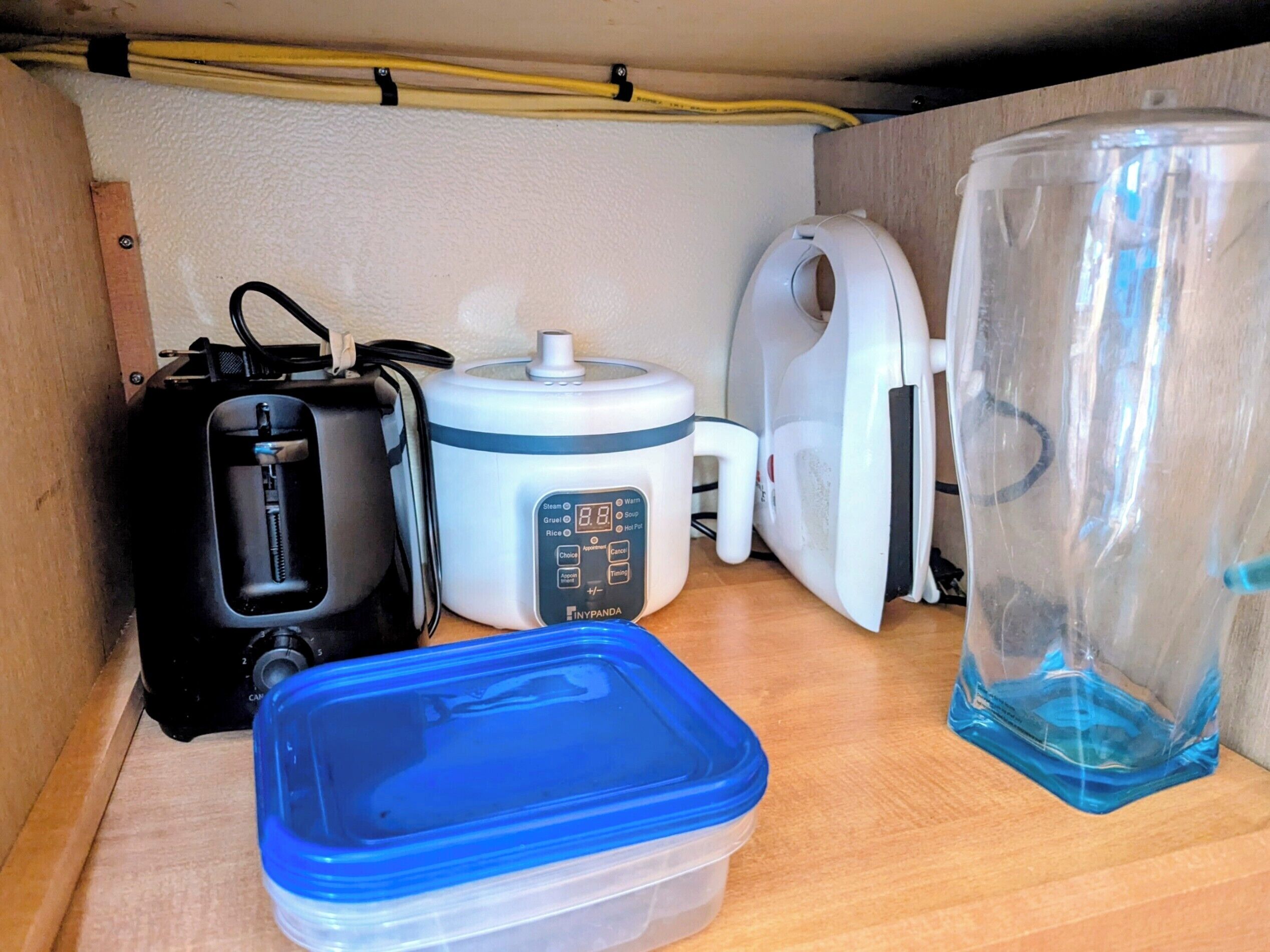 A kitchen area with a rice cooker, a toaster, a kettle, and a water container.