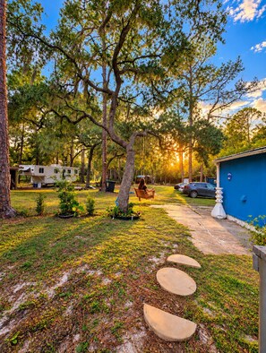 A campsite with a blue building, a covered picnic table, and a recreational vehicle. - Nice Camper Under the Stars • Free Parking • Fire Pit • Hammock • Pet-Friendly.  (Hawthorne)