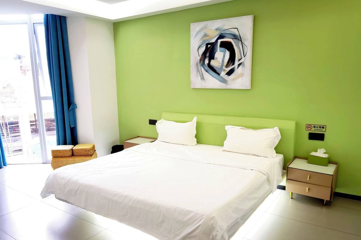 A modern hotel room with a large bed, green walls, and a painting above the bed.