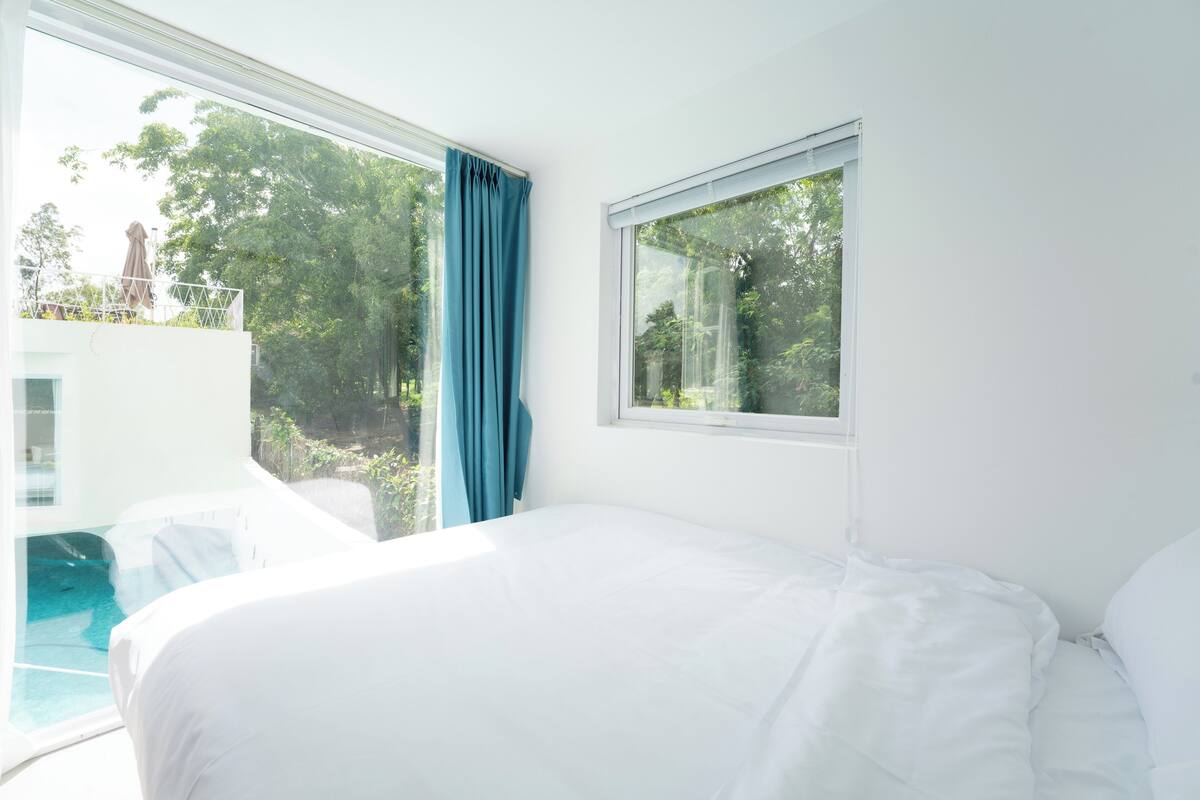 A bedroom with a large window, a bed, and a view of a swimming pool.