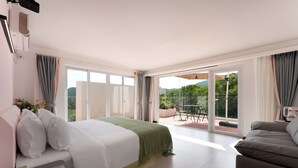Een moderne hotelkamer met een groot bed, een bank, een balkon met een tafel en stoelen, en een schuifdeur naar een terras.