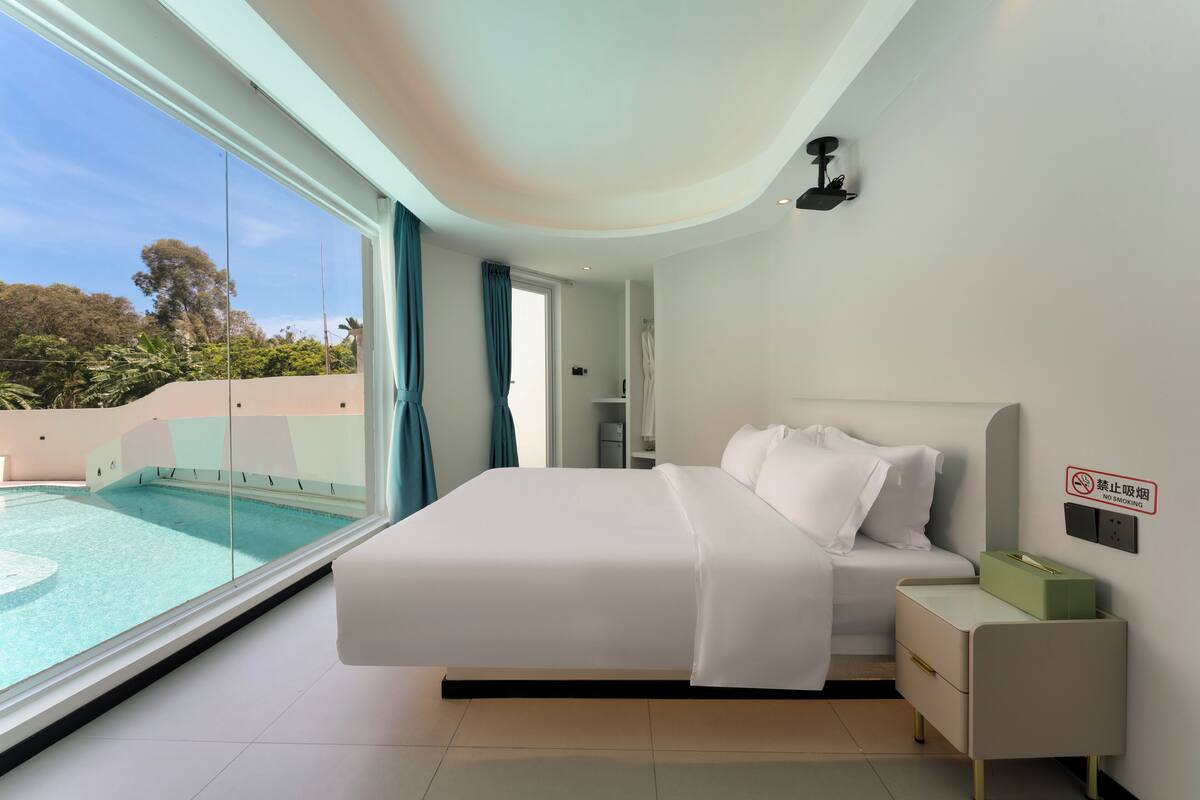 A modern bedroom with a large bed, a bedside table, a nightstand, and a view of a swimming pool.