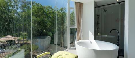 Un baño moderno con una bañera amplia, ducha con mampara de vidrio y vistas a un paisaje natural.