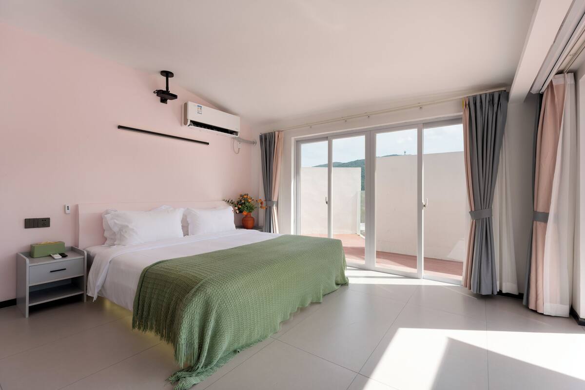 A modern bedroom with a large bed, a nightstand, a wall-mounted air conditioner, and a sliding glass door leading to a balcony.