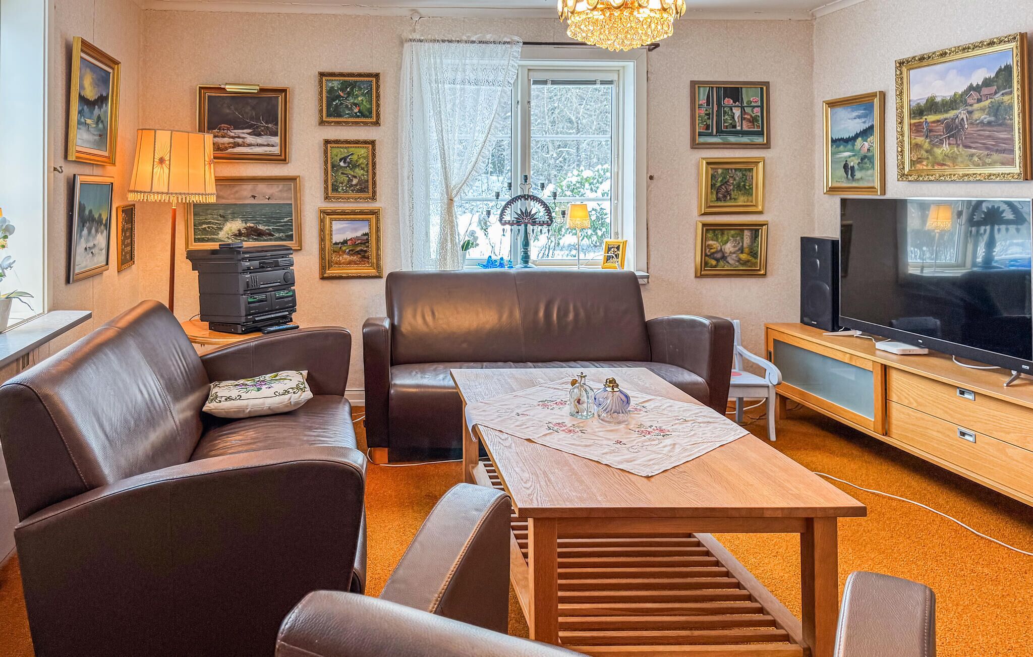 A living room with a sofa, a coffee table, a TV, and various framed pictures on the walls.