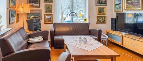 A living room with a sofa, a coffee table, a TV, and various framed pictures on the walls.