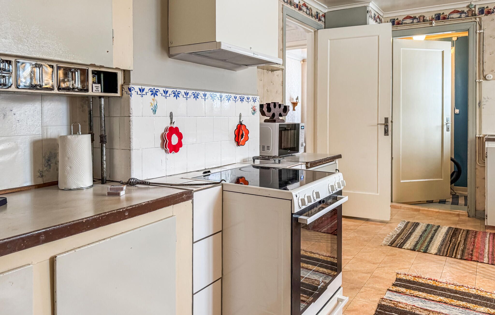 A kitchen with white cabinets, a stove, and a microwave. There are two red flower-shaped hooks on the wall.