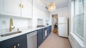 Ett modernt kök med vita skåp, en diskho i rostfritt stål, en gasspis och ett vitt kylskåp.