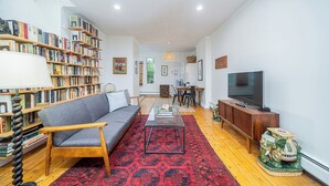Ett vardagsrum med en soffa, ett soffbord, en bokhylla, en tv och en mönstrad matta.