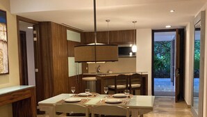 A modern dining area with a central table set for four, flanked by wooden cabinets and a kitchen in the background. - Grand Bliss 1 Bedroom Suite (Riviera Maya)