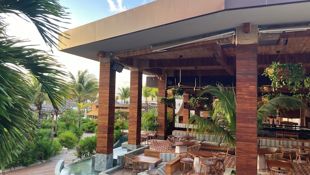 A covered outdoor area with wooden pillars, seating, and a water feature. - Grand Bliss 1 Bedroom Suite (Riviera Maya)