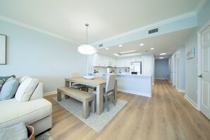 A modern kitchen with white cabinets, a wooden dining table, and a built-in island. - Coastal Calm Boardwalk 1601 • Remodeled 3BR Gulf-Front End Unit w/ Huge Balcony (Panama City Beach)