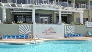 Area piscina con poltrone da relax blu, un cartello con la scritta The Boardwalk Beach Resort e un edificio bianco con balconi.