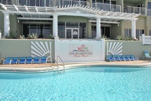 Un área de piscina con sillones reclinables azules, un letrero que indica The Boardwalk Beach Resort, y un edificio blanco con balcones.