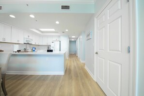 A modern kitchen with white cabinetry, a central island, and a wooden floor. - Coastal Calm Boardwalk 1601 • Remodeled 3BR Gulf-Front End Unit w/ Huge Balcony (Panama City Beach)