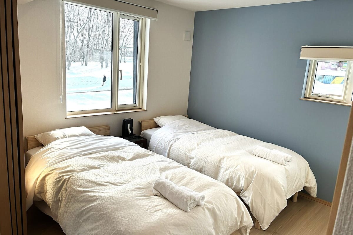 Un dormitorio con dos camas, una ventana que da a árboles y una mesita con una lámpara.