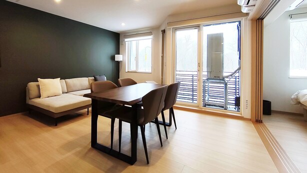 Un salon moderne avec un canapé, une table à manger et des chaises. Une grande fenêtre offre une vue sur l’extérieur.