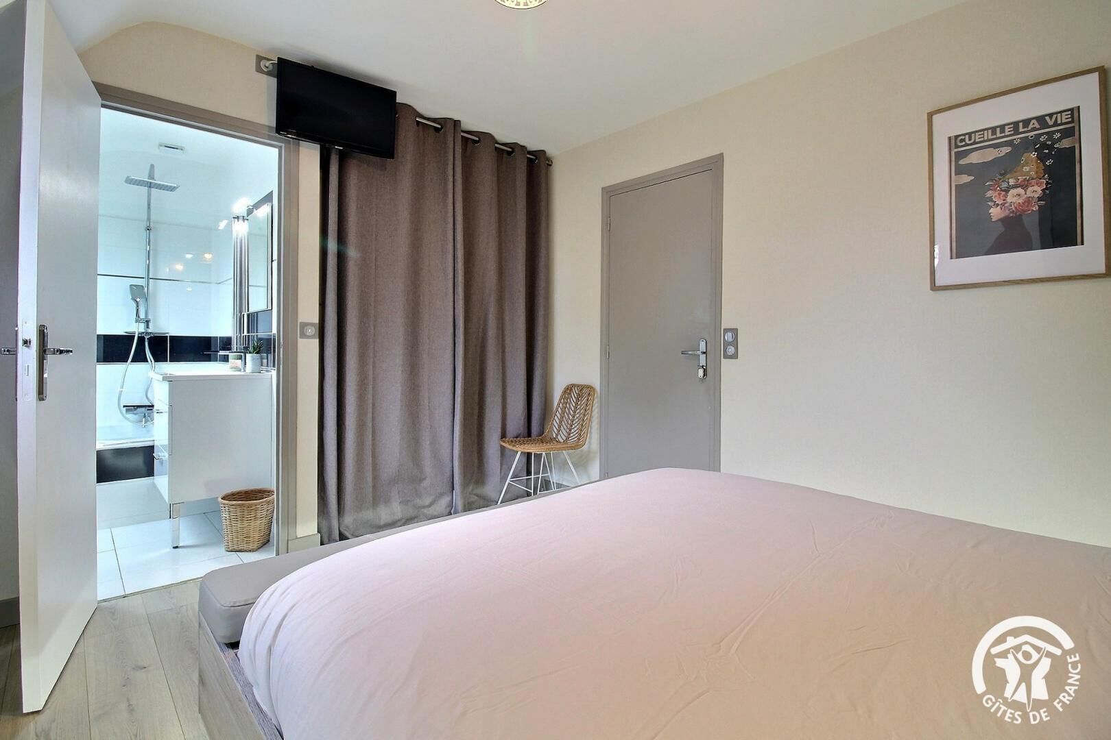 Un dormitorio con una cama, una silla, una puerta y un baño visible a través de una puerta abierta.