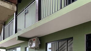 Un edifici modern amb façana verd, un balcó amb barana metàl·lica i una porta corredissa de vidre.