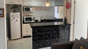 Una cocina moderna con armarios blancos, encimera de mármol negro, microondas y una lámpara colgante.