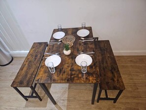A square wooden dining table with four white plates, cutlery, and glasses, centered with a pineapple decoration. - City Haven Manchester Apartment (Manchester)