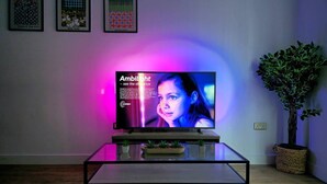 Una sala de estar con una televisión de pantalla plana sobre una mesa de centro de vidrio, una planta en maceta y cuadros en la pared.