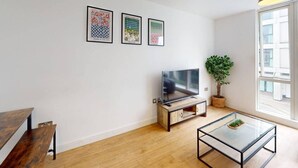Una sala de estar moderna con piso de madera, una mesa de centro de vidrio, un televisor sobre un mueble de madera y tres obras de arte enmarcadas en la pared.