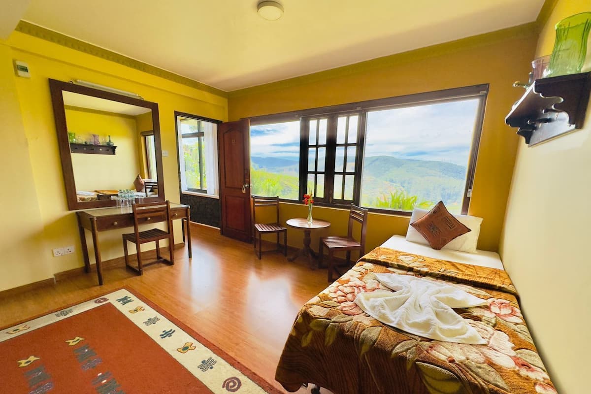 Ein Hotelzimmer mit Bett, Schreibtisch, Stuhl, einem kleinen Tisch und Blick ins Freie.