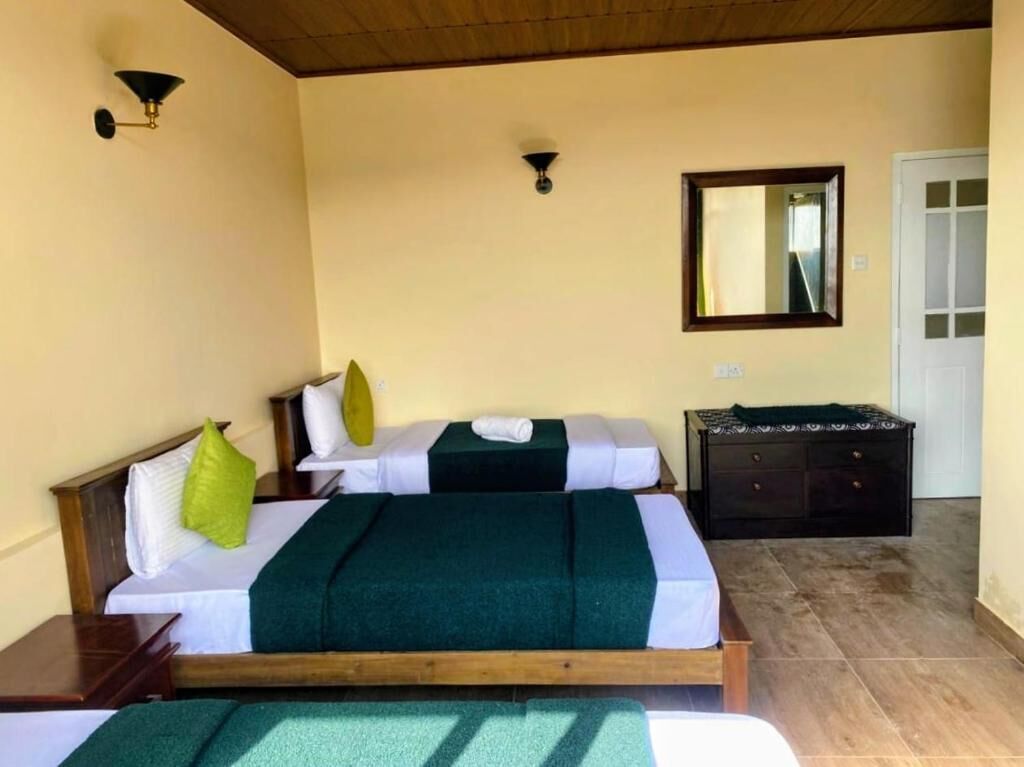 Une chambre avec deux lits, une tête de lit en bois, une commode sombre et un miroir au mur.